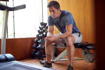 Man Anxious About Body Image Sitting On Weight Bench In Home Gym