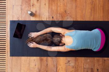 Overhead View Of Woman Stretching On Exercise Mat Using Digital Tablet