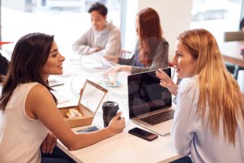 Group Of Young Businesswomen Sitting Around Table In Modern Workspace Having Working Lunch Meeting