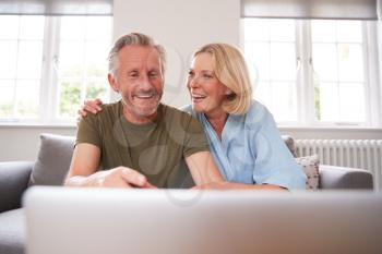 Senior Couple Sitting On Sofa In Lounge At Home Using Laptop Together