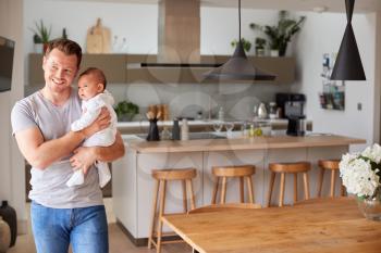 Portrait Of 3 Month Old Baby Daughter Being Held By Loving Father In Kitchen At Home