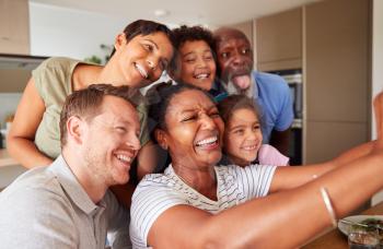 Multi-Generation Mixed Race Family Posing For Selfie As They Eat Meal Around Table At Home Together