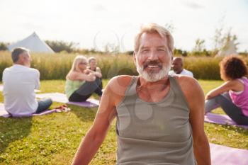 Portrait Of Mature Man On Outdoor Yoga Retreat With Friends And Campsite In Background