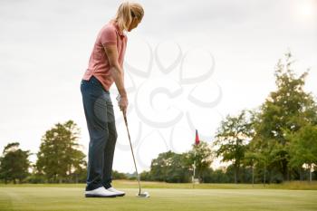 Rear View Of Female Golfer Putting Ball On Green