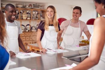 Male And Female Students Standing With Chopping Boards At Start Of Cookery Class In Kitchen