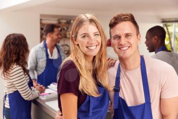 Portrait Of Smiling Couple Wearing Aprons Taking Part In Cookery Class In Kitchen