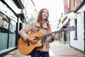 Female Musician Busking Playing Acoustic Guitar Outdoors In Street