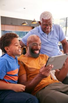 Multi-Generation Male African American Family Sitting On Sofa At Home Using Digital Tablet
