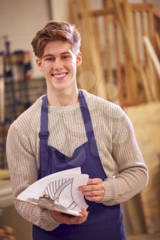 Portrait Of Male Student Studying For Carpentry Apprenticeship At College With Plans For Staircase