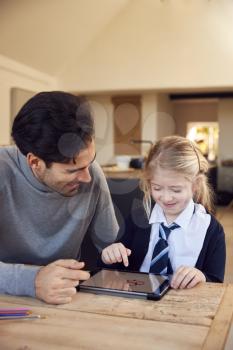 Father Helping Daughter Using Digital Tablet Wearing School Uniform With Homework At Table