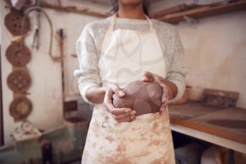 Close Up Of Female Potter Wearing Apron Holding Lump Of Clay In Ceramics Studio