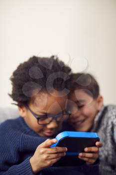 Two Boys Gaming Together On Hand Held Devices At Home