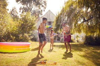 Family Wearing Swimming Costumes Having Water Fight With Water Pistols In Summer Garden