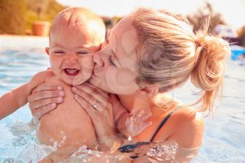 Mother With Baby Daughter Having Fun On Summer Vacation Splashing In Outdoor Swimming Pool