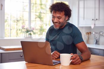 Mature Man In Kitchen Working From Home On Laptop Computer