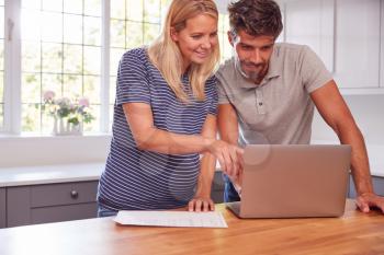 Couple With Pregnant Wife At Home Buying Products Or Services Online Using Laptop