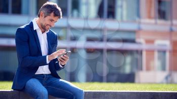 Businessman On A Break Sitting Outside Office Using Mobile Phone