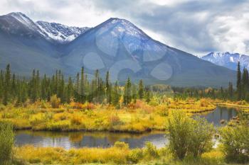 The picturesque bog surrounded by an autumn multi-coloured grass, on a background of ice mountains of the north