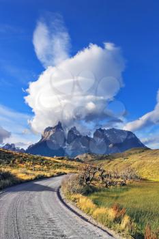 The Fantastic sunset in the Chilean Patagonia. Incredible clouds above the cliffs of Los Kuernos in national park Torres del Paine. A dirt road leads to the mountain range