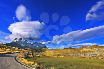The exceptional beauty of the sunset in the Chilean Patagonia. Fabulous clouds over cliffs Los Kuernos in national park Torres del Paine. The dirt road leads to the mountain range