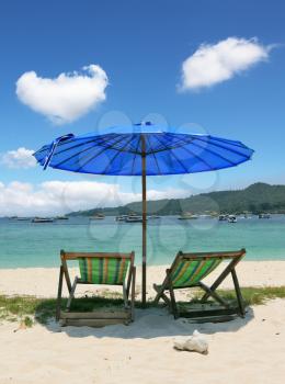 A picturesque dark blue beach umbrella and striped chaise lounges on white beach sand