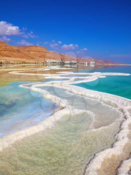 The path from salt picturesquely curls in salty water. Hotels are reflected in smooth water ashore. Israeli coast of the Dead Sea