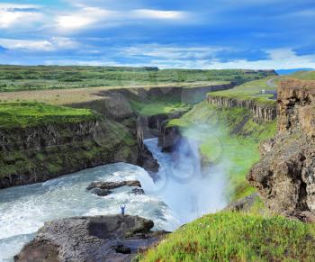 Delighted woman tourist on the shore of the huge waterfall Gyullfoss. Summer in Iceland