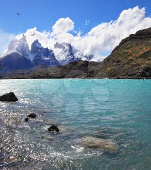 Magic beauty of Lake Pehoe. A strong wind blows turquoise waves on the lake, grand cliffs of Los Kuernos covered with snow and ice