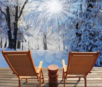 Christmas in the forest. Trees covered with snow, shine to the December winter sun. Comfortable wooden chairs and a small round table invite tourists to relax and enjoy the winter wonderland