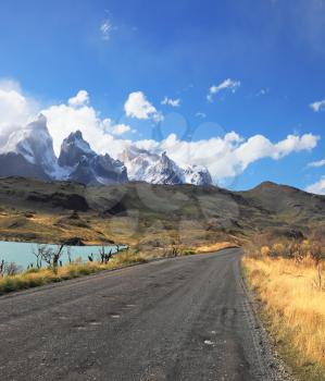 The gravel road along the shore of Lake Pehoe. The National Park Torres del Paine in Chile. In the distance are seen cliffs of Los Cuernos