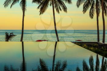 Delicate sunset on the popular resort island of Koh Samui. Palm trees reflected in smooth water of the pool on the beach