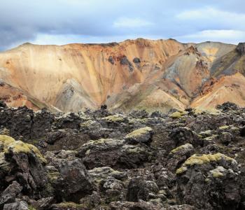 National Park Landmannalaugar in Iceland. Pieces of gray and black lava, sometimes covered with green moss. In the background - blue and orange rhyolite mountains