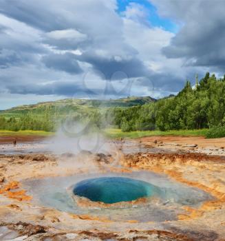 Magnificent geyser Strokkur in Iceland. Bowl-shaped fumarole depression in the ground with splashing hot water azure