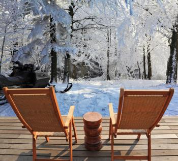 Christmas in the forest. Trees covered with snow. Comfortable wooden chairs and a small round table invite tourists to relax and enjoy the winter wonderland
