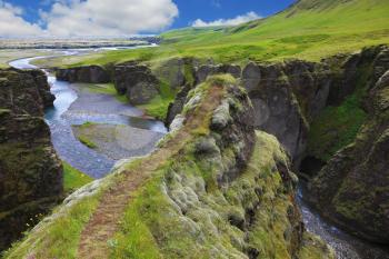 The picturesque canyon Fjadrargljufur;, rocks with yellowed grass and blue water of the river. Neverland Iceland