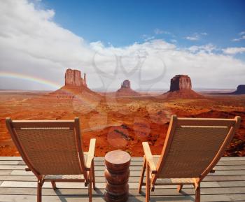Red sandstone in the valley of the Navajo. Famous rock - mitts crosses the rainbow. Two chairs - deck chairs on the wooden platform are for tourists