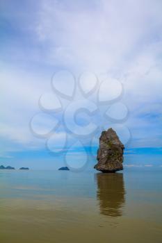 The haze of the warm sea - background for the huge stone cliff. Island Sail in the ocean. The island is reflected in the smooth surface of the water