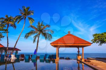 Rest of the Andaman Sea. Popular resort on the island of Koh Samui. Pool surrounded by palm trees on the sea beach. On the edge of the pool red sun canopy