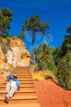 Middle-aged woman on the steps of photographing the park. Unique red and orange hills in the province of Languedoc - Roussillon, France