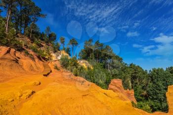 Unique red and orange hills in the province of Roussillon, France. Coniferous forests create a beautiful contrast with the color of ocher