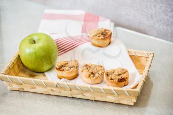 Magnificent portioned tartlet cakes with sweet stuffing. Professional baking. Background of wicker basket, white dish towel and green apple