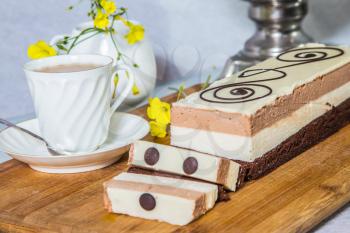 Three-layer chocolate cake, decorated with chocolate patterns. Beautiful cake Three-colate. Background - white vase with flowers and porcelain cup with hot tea. Professional bakery