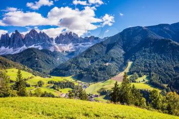 Lovely sunny autumn day. Odle mountain peaks and forested mountains surrounded by green Alpine meadows. Dolomites, Val de Funes valley