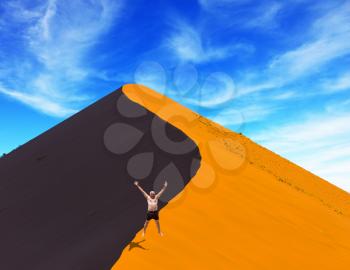 The man enthusiastically jumps on the crest of the dune. Purple and yellow dune of the Namib desert. Sunset. The concept of extreme and exotic tourism