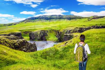  Green Tundra in summer. The elderly woman -  tourist with big backpack admiring the magnificent scenery. The concept of active northern tourism. The striking canyon in Iceland