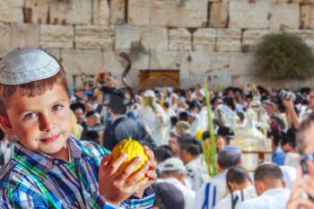 Beautiful Jewish boy in white skullcap, with etrog. Autumn Jewish holiday Sukkot. People in white Taliths pray at the Western Wall of the Temple 