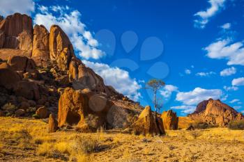 Nature reserve Spitzkoppe in Namibia. Picturesque stone arches are painted by iron oxides in red-orange color. Evening sun lengthens the shadows among the rocks