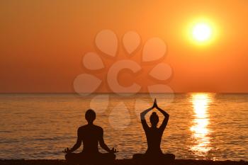 Silhouette of woman and man practicing yoga on the beach at sunrise