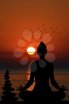 Silhouette of yogi in lotus position and a pile of stone at sea shore at sunset