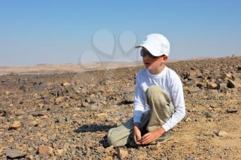Royalty Free Photo of a Boy Picking Up Stone in the Desert